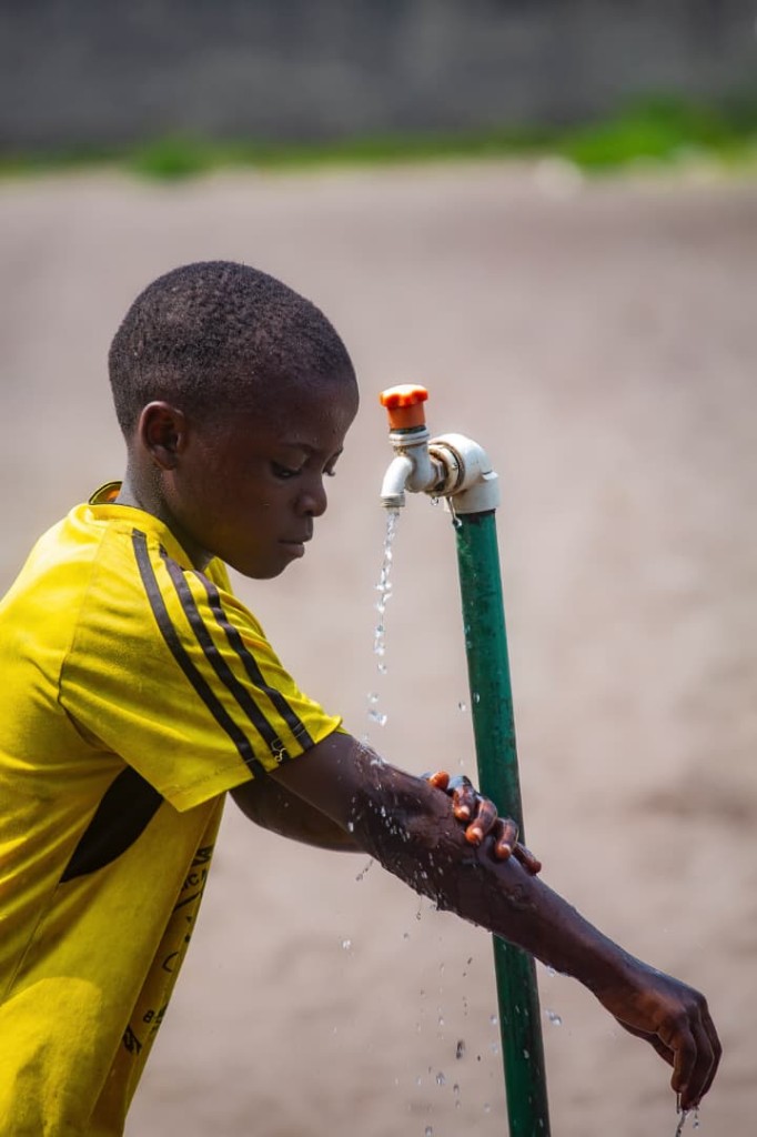 A child washing at an outdoor tap with clean running water
