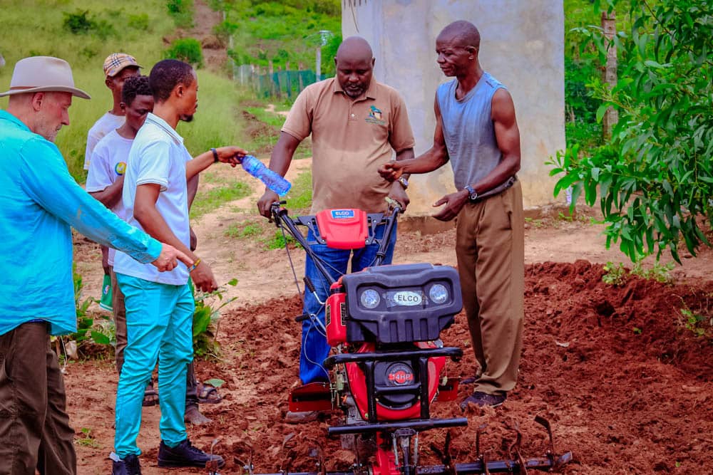 Farm partners demonstrating a walk-behind power tiller on prepared soil