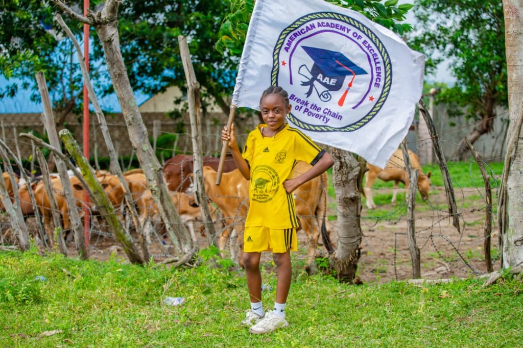 Student holding an American Academy of Excellence flag beside a pasture with cattle